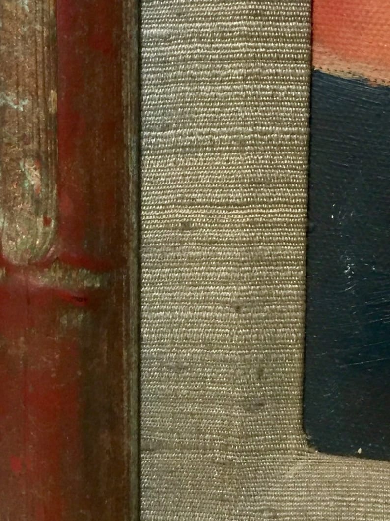 May include: Close-up of a red, brown, and gold wooden frame with a beige fabric lining. The fabric has a woven texture.