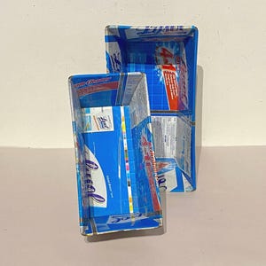 May include: Two blue rectangular containers made from recycled cleaning product boxes. The boxes are stacked on top of each other. The boxes have the words "4 in 1" and "Lysol" printed on them.