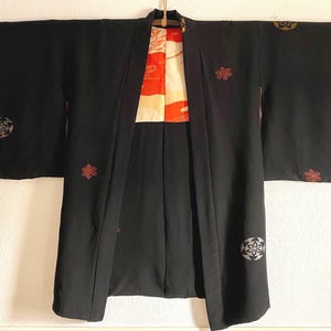 Könnte beinhalten: Eine schwarze japanische Hanten-Jacke mit roten und goldenen Stickereien. Die Jacke hat ein traditionelles Design mit einem Blumenmuster und einem geometrischen Muster.