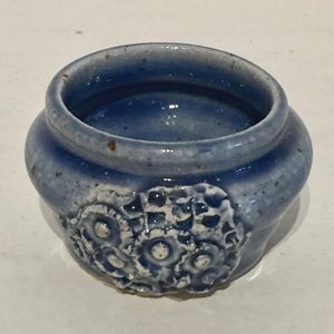 以下が含まれることがあります： 白いテクスチャのあるデザインが施された、小さな青い陶器の鉢。鉢は丸みを帯びた形をしていて、開口部が広い。