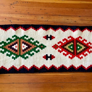 May include: A white runner rug with a black border and red, green, and brown geometric patterns.