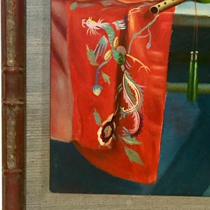 May include: A framed painting of a still life with a red fabric with a green and yellow embroidered dragon design, a wooden flute, and a blue bowl.
