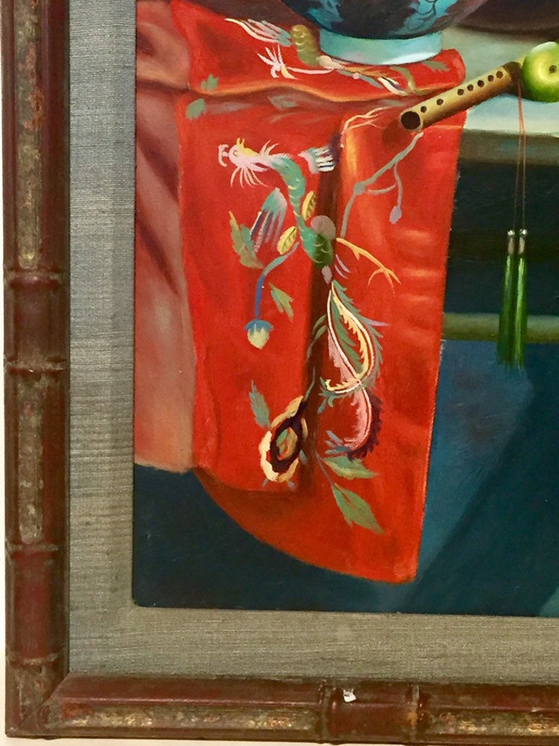 May include: A framed painting of a still life with a red fabric with a green and yellow embroidered dragon design, a wooden flute, and a blue bowl.