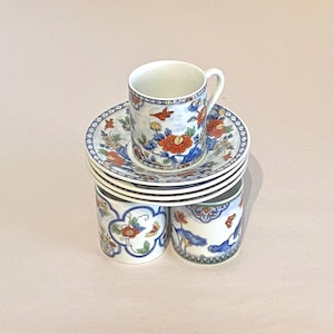 May include: A set of six white porcelain teacups and saucers with a floral pattern in shades of blue, red, and green. The cups and saucers feature a delicate floral design with intricate details.