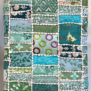May include: A square patchwork cushion with a variety of green, blue, and white fabrics. The cushion is made of different pieces of fabric sewn together in a patchwork design. The fabric is embroidered with various patterns, including circles, flowers, and leaves.