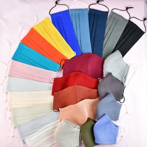 May include: A collection of 18 face masks in various colors and fabrics, including solid colors, patterns, and textures. The masks are arranged in a semi-circle on a pink background.