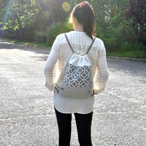May include: A gray and white geometric pattern drawstring backpack. The top portion is white, the middle section features a gray and white geometric design, and the bottom is solid gray. The backpack has gray drawstrings.