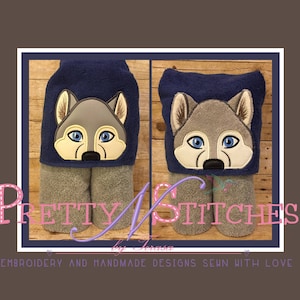 May include: Two navy blue hooded towels with wolf faces. The wolf faces have gray fur, blue eyes, and black noses. The towels are gray and have a decorative border. The text "Pretty N Stitches" is visible.