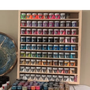 May include: A wooden shelf unit with multiple rows of small jars filled with colorful glitter. The jars have silver lids and a black logo that says "POPS".