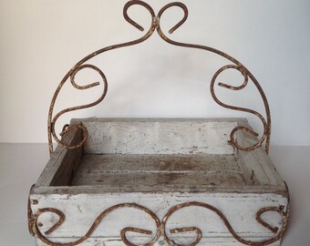 May include: A white wooden tray with a rusty metal frame. The frame has a decorative design with swirls and loops. The tray is perfect for displaying small items or serving snacks.