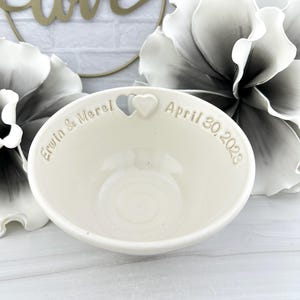 May include: White ceramic bowl with a heart cutout and the inscription "Erwin & Merel April 30, 2023".