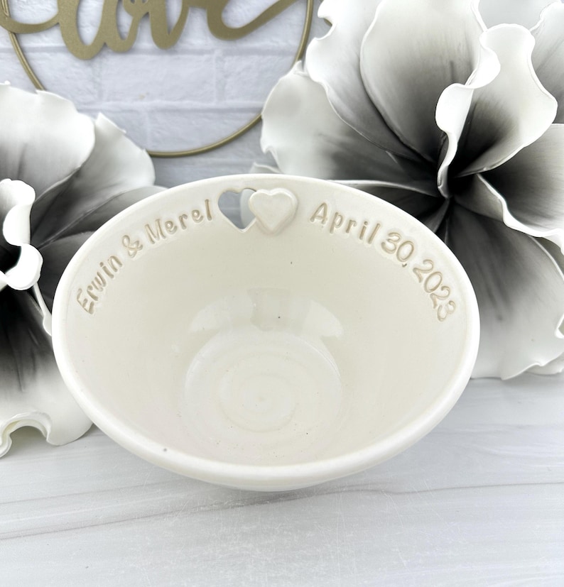May include: White ceramic bowl with a heart cutout and the inscription "Erwin & Merel April 30, 2023".