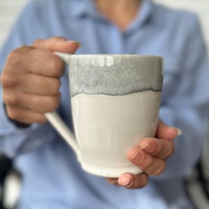 May include: A white ceramic mug with a gray glaze on the top half. The mug has a rounded handle.