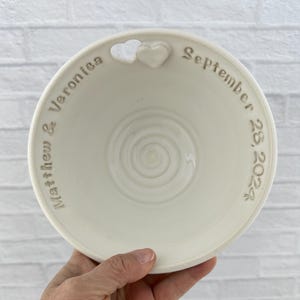 May include: White ceramic bowl with a heart-shaped cutout and the inscription "Matthew & Veronica September 28, 2024".
