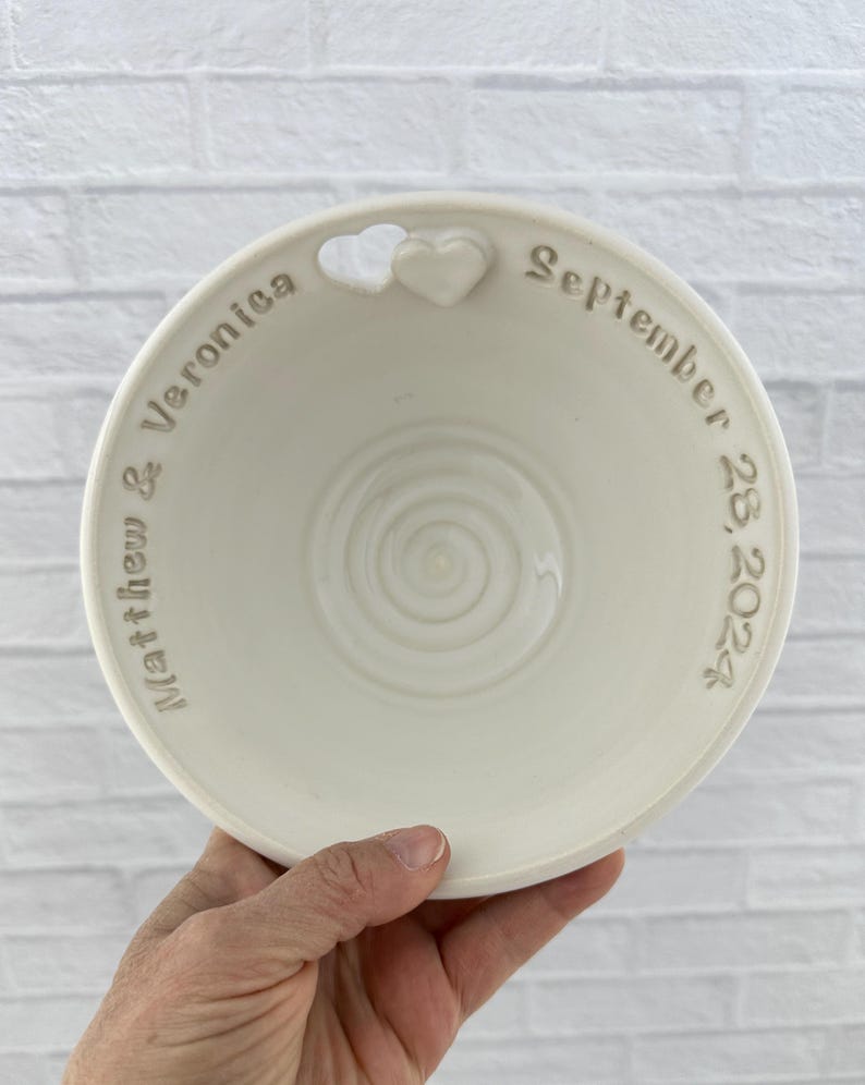May include: White ceramic bowl with a heart-shaped cutout and the inscription "Matthew & Veronica September 28, 2024".