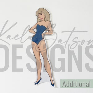 May include: A paper doll cutout of a woman in a blue swimsuit with blonde hair. The doll has a stand and is labeled "Additional Doll". The design includes the text "Kaela Batson DESIGNS".