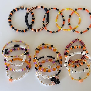 May include: A collection of Halloween-themed beaded bracelets featuring orange, black, white, and purple colors. The bracelets include clay discs, faceted beads, and letter beads spelling out phrases like SPOOKY, HEY BOO, and FREAKIN, with ghost and pumpkin charms.