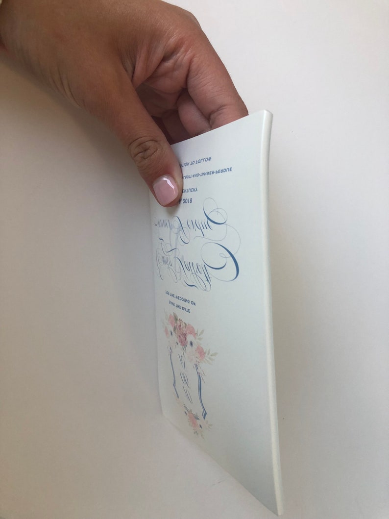 May include: A white wedding invitation with blue and pink floral designs. The invitation includes the names "Jamie & Megan" and the date "July 21, 2018".