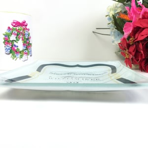May include: A clear glass serving tray with a black and gold design. The tray has a white background with a decorative design in the center. The tray is sitting on a white surface.