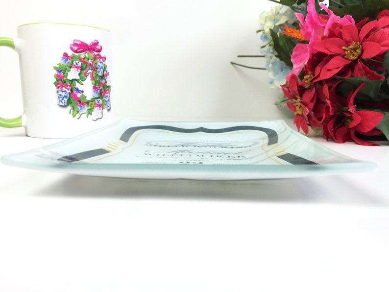 May include: A clear glass serving tray with a black and gold design. The tray has a white background with a decorative design in the center. The tray is sitting on a white surface.