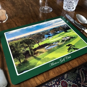 May include: A green placemat with a photo of a golf course and the text "Merion Golf Club".