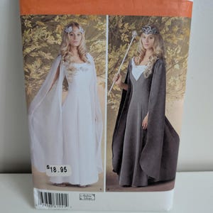 May include: Simplicity sewing pattern 1551, size U.S. 16-24, features two floor-length dress variations with capes. One dress is white with a square neckline, and the other is dark gray with a white bodice insert and a matching scepter.