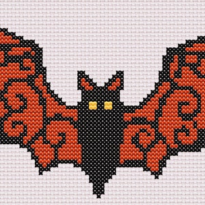 May include: A black bat with orange wings, stitched in a cross-stitch pattern. The bat has yellow eyes.