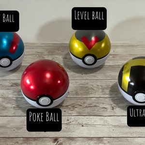 May include: Four colorful Poke Balls, including Great Ball, Level Ball, Poke Ball, and Ultra Ball. Each ball is round with a white base and a colored top, with black text labels. The balls are on a wooden surface.