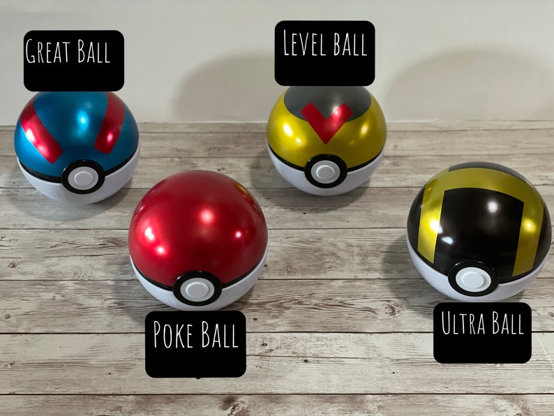 May include: Four colorful Poke Balls, including Great Ball, Level Ball, Poke Ball, and Ultra Ball. Each ball is round with a white base and a colored top, with black text labels. The balls are on a wooden surface.