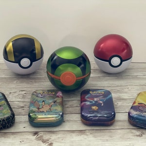 May include: A collection of Pokemon-themed items, including several spherical Poke Balls in black and gold, green and black, and red and white. Rectangular tins with Pokemon characters are also present, featuring various designs and colors.