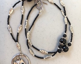 May include: A black beaded necklace with silver-toned accents and a pendant. The pendant features a heart-shaped black stone and an owl design with rhinestone accents. The necklace has a toggle clasp.