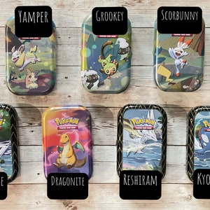 May include: Seven rectangular metal tins featuring Pok&eacute;mon characters and the Pok&eacute;mon Trading Card Game logo. Each tin has a different character name on a black label: Yamper, Grookey, Scorbunny, Zarude, Dragonite, Reshiram, and Kyogre.