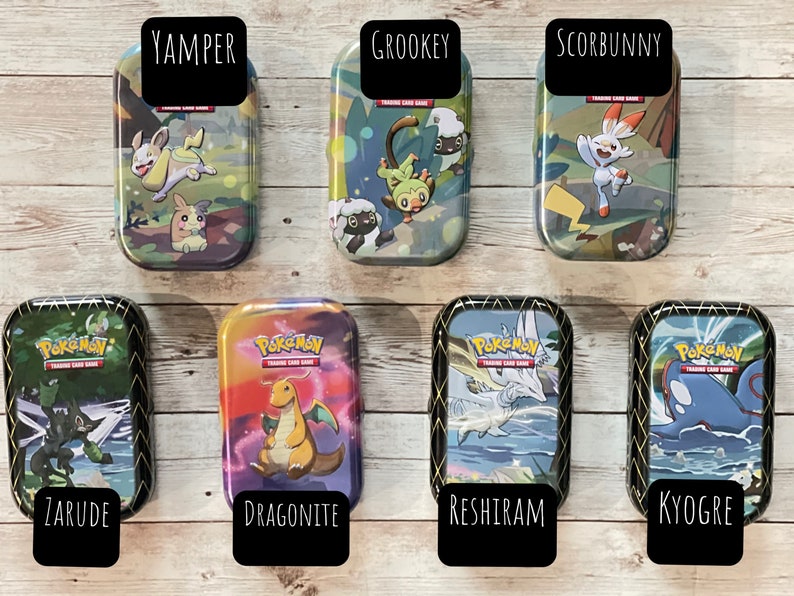 May include: Seven rectangular metal tins featuring Pok&eacute;mon characters and the Pok&eacute;mon Trading Card Game logo. Each tin has a different character name on a black label: Yamper, Grookey, Scorbunny, Zarude, Dragonite, Reshiram, and Kyogre.