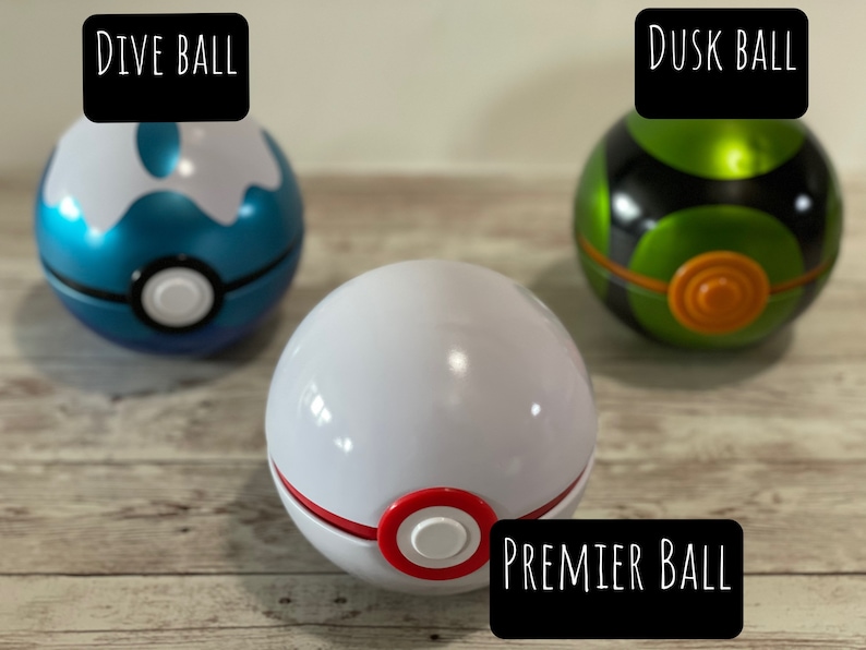 May include: Three colorful Pok&eacute; Balls: a blue and white Dive Ball, a white Premier Ball with red accents, and a green and black Dusk Ball. Each ball has a white button in the center. The text "DIVE BALL", "PREMIER BALL", and "DUSK BALL" are displayed.
