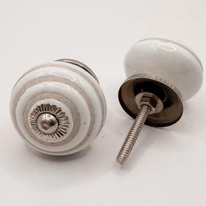 May include: Two white and gray striped ceramic cabinet knobs with silver hardware. One knob has a decorative silver base. The other knob has a threaded screw for installation. The knobs are for home decor.