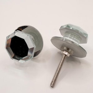 May include: Two clear, faceted glass cabinet knobs with silver-colored hardware. The knobs have an octagonal shape and are designed for easy installation. The hardware includes a threaded bolt and a circular base.