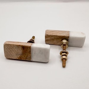 May include: Two rectangular cabinet knobs. Each knob is half light wood and half white marble. The knobs have brass hardware and are designed for easy installation. The knobs are a decorative accent for furniture.