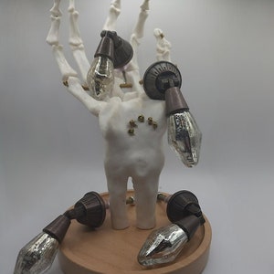 May include: Four antique-style cabinet knobs with a silver finish and a dark brown metal base. The knobs are displayed on a wooden base and a skeletal hand.