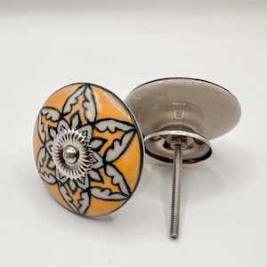 May include: Two decorative cabinet knobs with a floral design. The knobs have a bright orange background with a black and white floral pattern. Each knob has a silver-colored metal base and screw.
