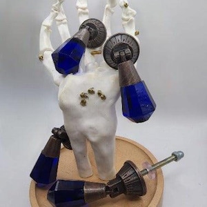 May include: Four blue glass cabinet knobs with antique brass hardware. The knobs are attached to a skeletal hand, which is holding them up.