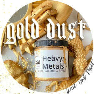 May include: A gold metallic paint jar labeled "Heavy Metals Metallic Gilding Paint" with the brand name "Gold Dust" in a gold circle with the text "Wise Owl Paint" below.