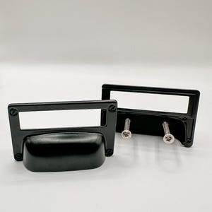 May include: Two black metal drawer pulls with a rectangular label holder and a curved handle. One pull is shown with screws attached. The pulls are on a white background. The text "SWEET COTTONWOOD" is at the bottom.