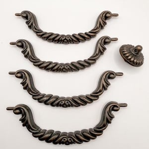 May include: Four antique bronze-colored drawer pulls and a matching knob. The pulls have a curved, ornate design with a rope-like center and decorative ends. The knob is round with a fluted edge. The Sweet Cottonwood logo is visible at the bottom.
