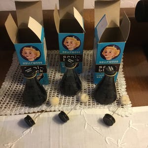 May include: Vintage Hollywood Sani-Black liquid wax bottles with applicators and boxes. The black bottles have gold accents and are accompanied by small, round applicators. The boxes are blue with a blonde woman's portrait and the text "Hollywood Sani-Black".