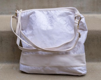 Bolso tipo hobo blanco suave con sutiles detalles de monograma: elegancia sin esfuerzo para usar de día y de noche.