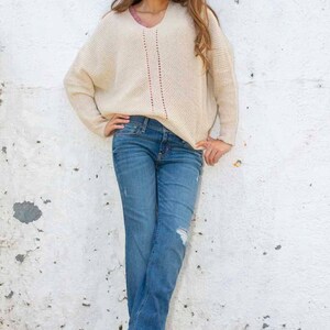 May include: A woman wearing a cream-colored sweater with a red and white design, blue jeans, and blue sandals.