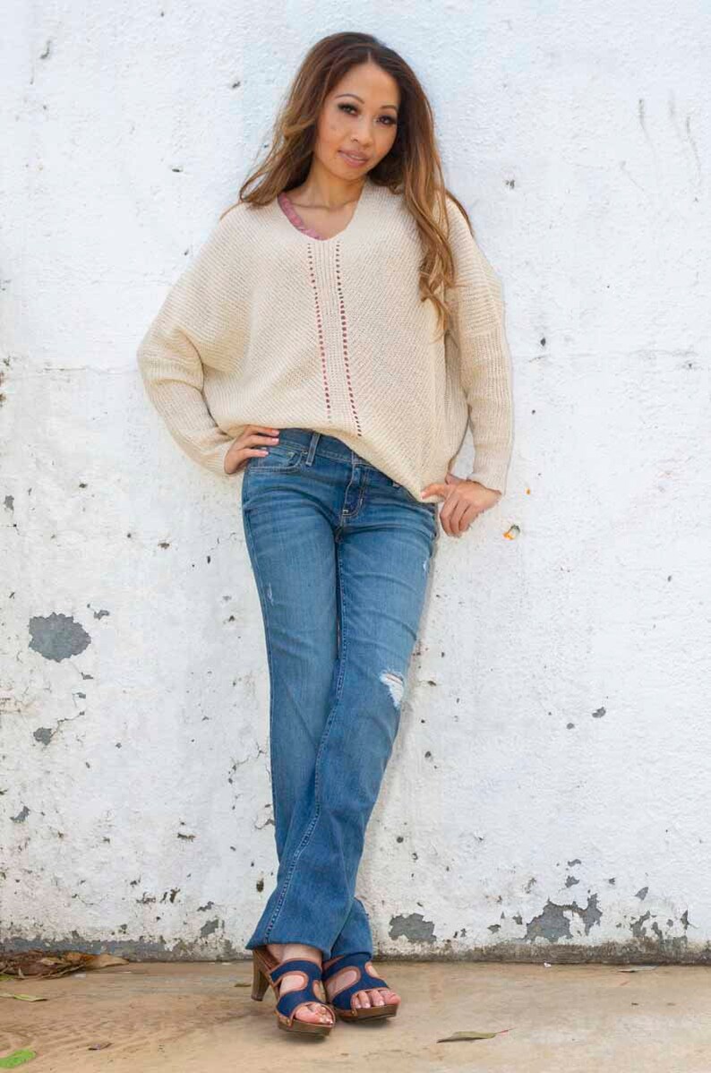 May include: A woman wearing a cream-colored sweater with a red and white design, blue jeans, and blue sandals.