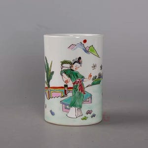 Puede incluir: Cilindro de cerámica blanca con un diseño pintado a mano de inspiración asiática. La obra de arte representa a una mujer con una túnica verde, montañas y elementos florales. El diseño es en tonos verdes, rojos, rosas y azules.