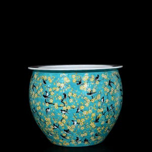 May include: A round, turquoise ceramic planter with a white rim. The planter is decorated with a pattern of yellow flowers and black birds. The planter is a decorative item.