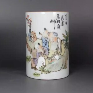 Può includere: Vaso cilindrico in ceramica bianca con una scena dipinta a mano di figure in abiti tradizionali. L'opera d'arte comprende un paesaggio con alberi, rocce e un piccolo vaso con fiori. Calligrafia visibile sul lato.